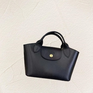 May include: A black handbag with two rounded handles and a flap closure. The bag has a textured surface and a gold-coloured button on the flap. The bag is a tote style.
