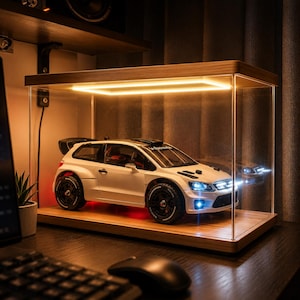 May include: A white scale model rally car with black wheels and a rear spoiler displayed inside a rectangular clear acrylic case with a wooden base and an integrated rectangular LED light strip illuminating the interior from above.