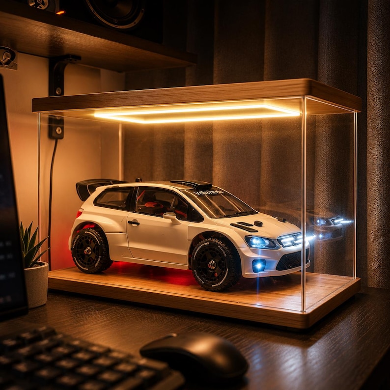 May include: A white scale model rally car with black wheels and a rear spoiler displayed inside a rectangular clear acrylic case with a wooden base and an integrated rectangular LED light strip illuminating the interior from above.