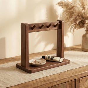 May include: A dark brown wooden key holder with five hooks, a small dish, and a tube of cream. The key holder is rectangular with a vertical frame and is sitting on a wooden surface. The dish contains several coins.