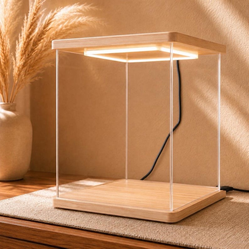 May include: A square display case featuring a light-colored wooden base and top, connected by four clear acrylic vertical supports. An integrated square LED light strip is recessed into the underside of the wooden top, casting a warm glow downward.