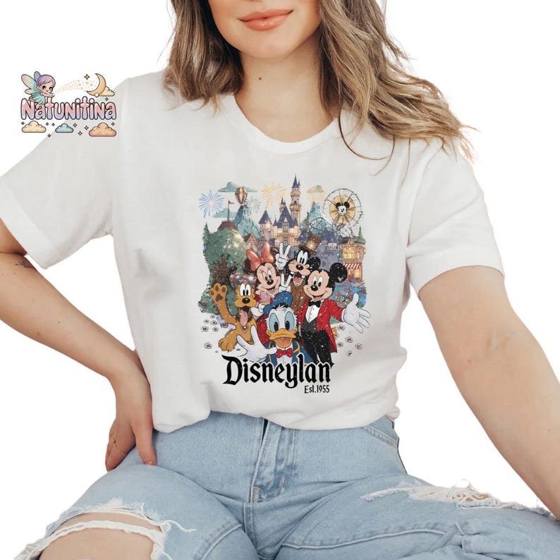 May include: White t-shirt featuring a colorful graphic of Disney characters, including Mickey Mouse, Minnie Mouse, and Donald Duck, in front of a castle and fireworks display. The word "Disneyland" is printed below the graphic.