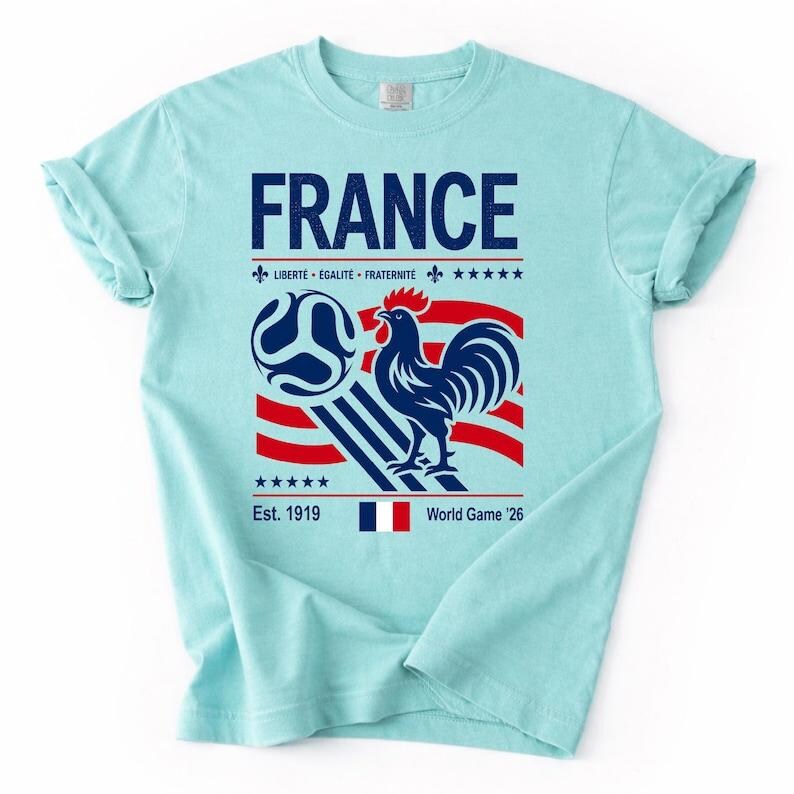 May include: A light blue t-shirt featuring a graphic print with the text FRANCE, LIBERT&Eacute; &Eacute;GALIT&Eacute; FRATERNIT&Eacute;, Est. 1919, and World Game '26. The design includes a blue rooster, a soccer ball, red and white stripes, five stars, and a French flag.