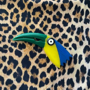 May include: A yellow, blue, and green toucan-shaped hair clip with a black eye.