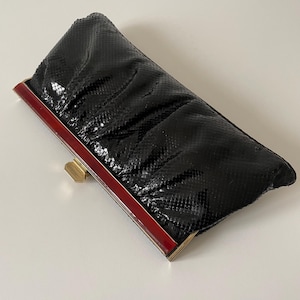 Peut inclure: Pochette noire avec un motif peau de serpent. Le cadre rectangulaire est rouge avec des accents métalliques dorés. La pochette se ferme avec un fermoir doré.