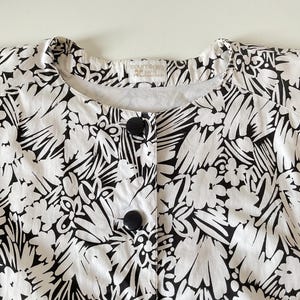 May include: A white and black floral print jacket with large black buttons. The jacket has a round neckline and a Courreges Paris label.