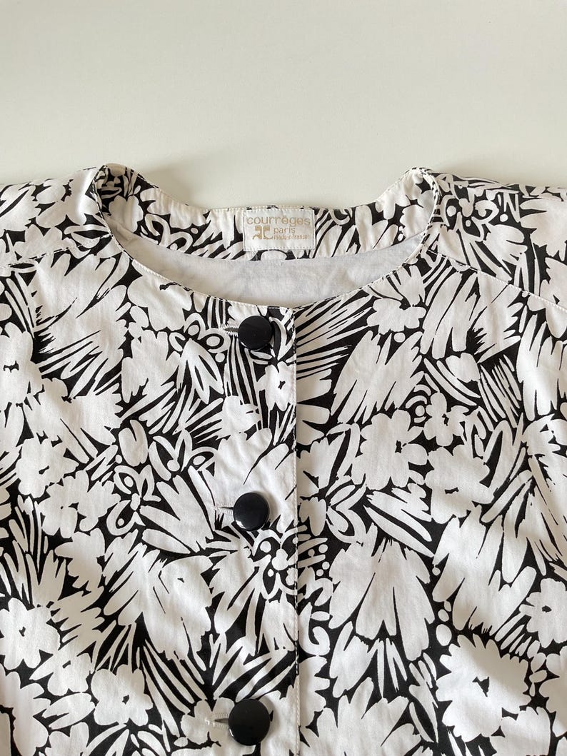 May include: A white and black floral print jacket with large black buttons. The jacket has a round neckline and a Courreges Paris label.