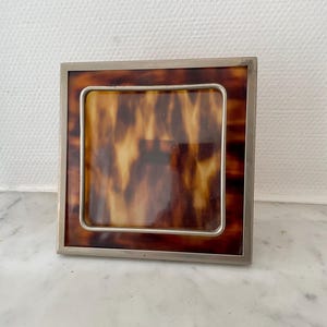 May include: A white ceramic mug with a black handle and the text "But First, Coffee" in a black, handwritten-style font. The mug is on a white surface.