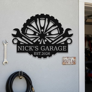 May include: Black metal garage sign with the text "NICK'S GARAGE EST.2026" and a gear and wrench design. A Route 66 sign is below the garage sign. A wrench and a coiled hose are also visible.