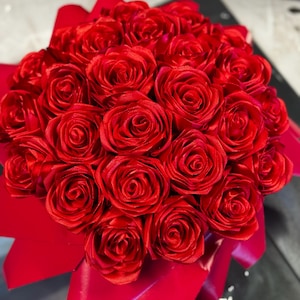 以下が含まれることがあります： 赤いサテンのバラの花束。芸術的にアレンジされ、お揃いの赤いリボンで飾られています。 バラはきつく巻かれており、ふっくらとした豪華な外観を作り出しています。 全体的なプレゼンテーションはエレガントで、贈り物に最適です。