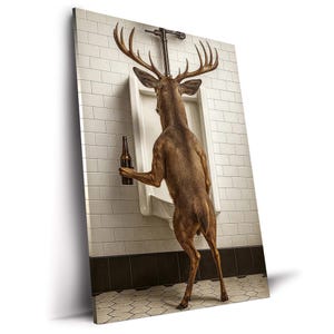 May include: A humorous art print depicts a deer in a bathroom, holding a beer bottle while standing at a urinal. The deer is brown with large antlers. The bathroom has white tile walls and a black and white tiled floor.