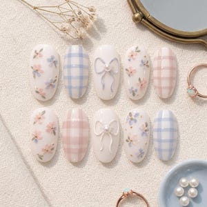 May include: A set of ten press-on nails featuring a white base with various designs including light blue and pink plaid patterns, small hand-painted floral motifs, and raised 3D bows accented with a single small white pearl bead on each bow.