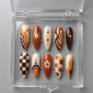 May include: A set of ten almond-shaped press-on nails arranged in a clear plastic storage case. The nails feature a color palette of cream, tan, orange, and dark brown, with designs including wavy lines, a sun, stars, checkers, and flowers.
