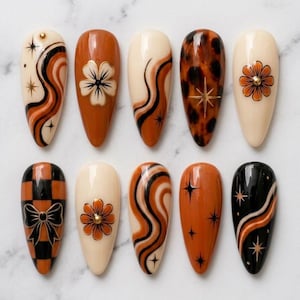 May include: A set of ten almond-shaped press-on nails featuring a color palette of cream, burnt orange, and black. Designs include wavy lines, starbursts, a flower with a gold stud, a leopard print pattern, and a checkered background with a bow.