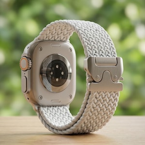 Puede incluir: Un reloj inteligente plateado con un sensor circular en la parte posterior, con una correa de nailon trenzado gris claro asegurada por una hebilla metálica con doble cierre. El lateral de la caja muestra una corona digital con un acento naranja.