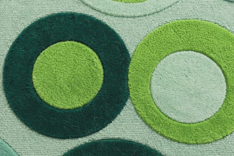Op de afbeelding: Een getextureerd tapijt met een herhalend patroon van grote cirkels in verschillende tinten groen. Het ontwerp bevat donker bosgroene, levendig limoengroene en zachte mintgroene cirkelvormen tegen een lichtgroene achtergrond.