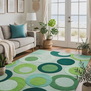 Op de afbeelding: Een rechthoekig vloerkleed met een geometrisch patroon van overlappende cirkels in diverse groentinten, waaronder bosgroen, limoengroen en mint. Het kleed heeft een getextureerde pool en bedekt een deel van de houten vloer in de kamer.