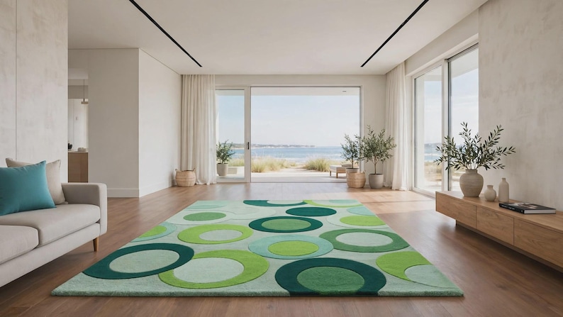 Op de afbeelding: Een rechthoekig vloerkleed met een herhalend patroon van overlappende cirkels in diverse groentinten, waaronder limoen, bosgroen en mint. Het kleed ligt op een lichte houten vloer in een kamer met witte muren en grote raampartijen.