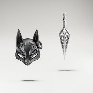 May include: A black fox mask and a silver dagger pendant, both embellished with sparkling gemstones. The mask has intricate details and a ring on the side. The dagger has a detailed handle and a sharp, pointed blade. The items are set against a white background.