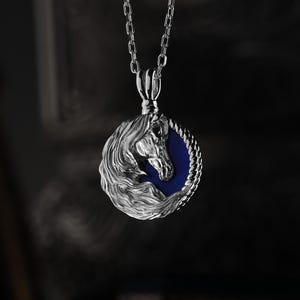 May include: A silver pendant necklace featuring a detailed horse head design. The horse head is set against a blue background within a circular frame. The necklace has a delicate chain.