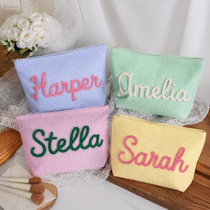 May include: Four rectangular zipped pouches with vertical pinstripes in blue, green, pink, and yellow. Each pouch features a name embroidered in cursive script: Harper in pink, Amelia in white, Stella in green, and Sarah in pink.