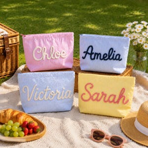 Può includere: Quattro pochette rettangolari con cerniera in tessuto seersucker rosa, azzurro e giallo. Ogni pochette presenta un nome ricamato in corsivo: Chloe in bianco, Amelia in blu navy, Victoria in bianco e Sarah in rosa.