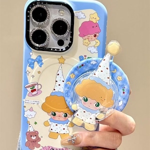 May include: A light blue phone case with a whimsical design featuring cartoon characters, stars, and clouds. The case has a matching pop socket with a cartoon character. The brand name "Y2kXCases" is visible at the top.
