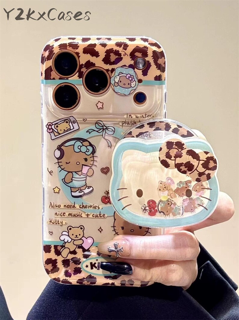 Puede incluir: Funda transparente para tel&eacute;fono con dise&ntilde;o de estampado de leopardo y tem&aacute;tica de Hello Kitty. La funda presenta un agarre emergente con un dise&ntilde;o de Hello Kitty y una secci&oacute;n transparente con dijes flotantes. El texto en la funda dice "Also need cherries, nice music + cute Kitty."