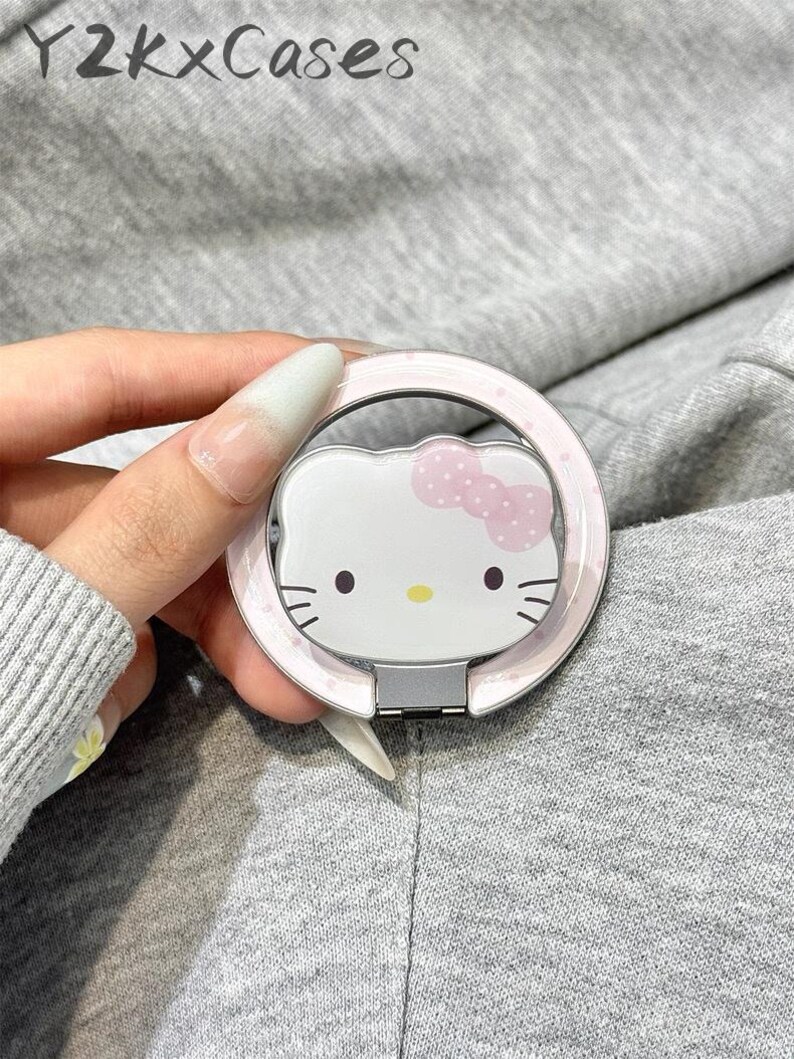 May include: A white and pink phone ring holder featuring the Hello Kitty character. The ring holder has a pink polka dot border and a silver hinge. The text "Y2k x Cases" is visible in the background.