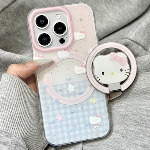May include: A pink and blue iPhone case with a Hello Kitty design. The case features a light pink border around the camera and a matching ring holder with a Hello Kitty face. The case has a gingham pattern and star accents.