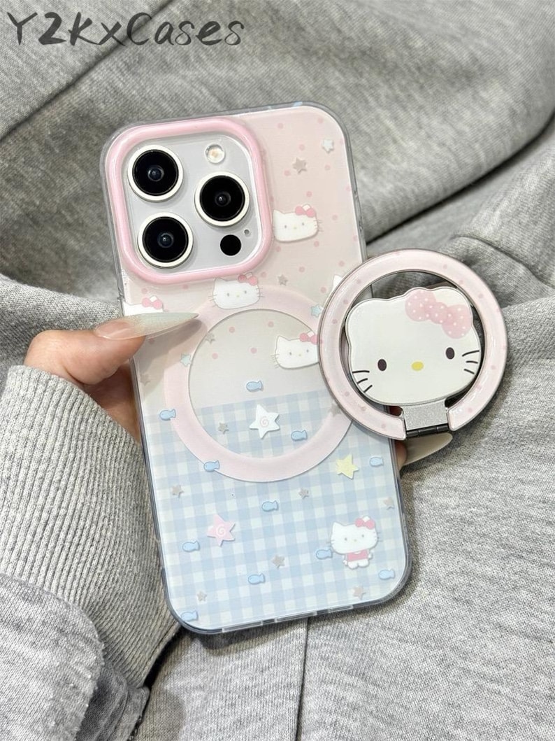 May include: A pink and blue iPhone case with a Hello Kitty design. The case features a light pink border around the camera and a matching ring holder with a Hello Kitty face. The case has a gingham pattern and star accents.