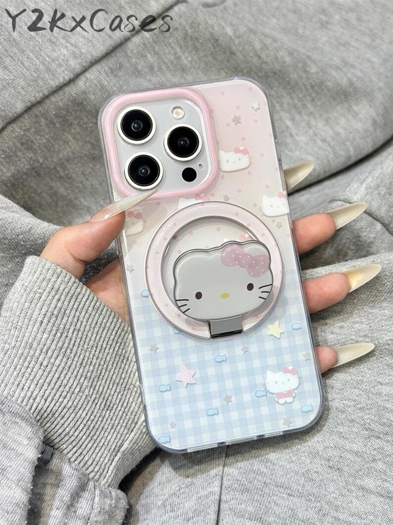 May include: Clear phone case with a pink and blue Hello Kitty design. The case features a pink border around the camera and a matching ring holder with a Hello Kitty face. The background has a pattern of stars, bows, and a gingham design. The text "Y2kxCases" is at the top.