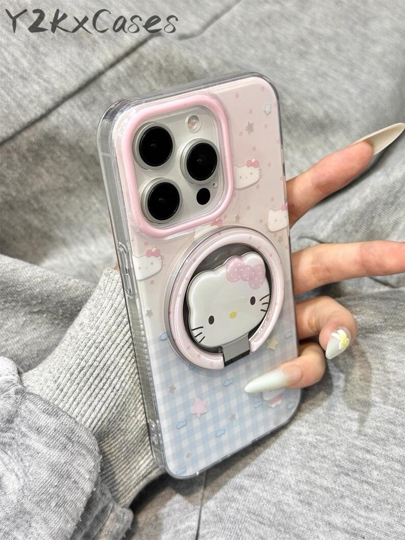 May include: Clear phone case with a pink and blue design featuring Hello Kitty characters. The case has a pink ring holder with a Hello Kitty face. The phone case has the text "Y2kXCases" at the top.