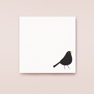 Op de afbeelding: Een wit notitieboekje met een geruit papier en een zwart silhouet van een vogel met een gele snavel.