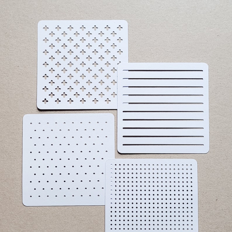 May include: Four white stencils with different patterns. One stencil has a repeating cross design, another has horizontal lines, and two have dot patterns of varying densities. The stencils are square with rounded corners.