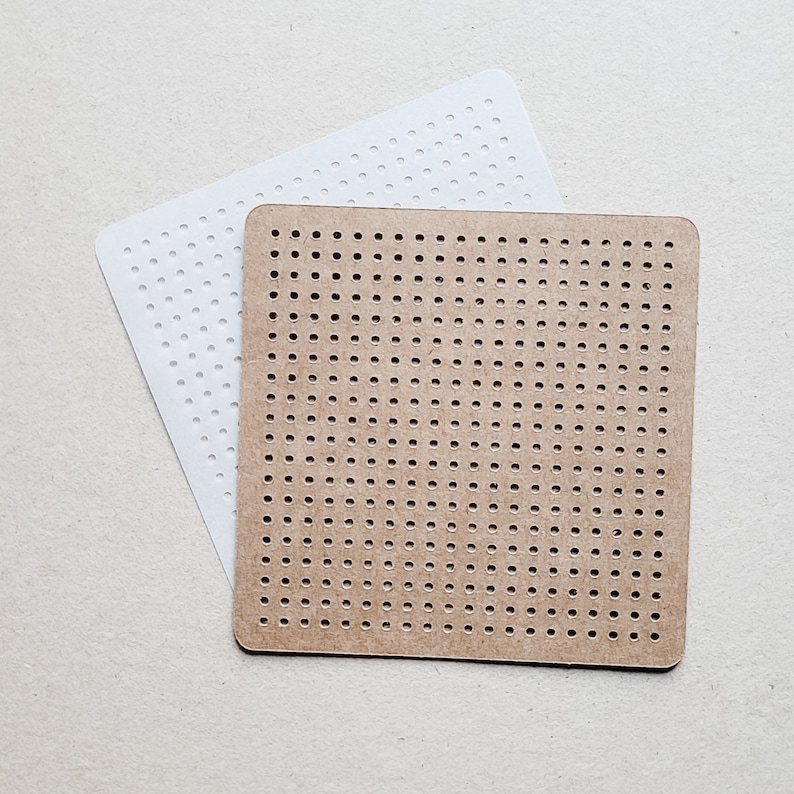 May include: Two square pegboards, one white and one brown, are displayed. Both pegboards have a grid of evenly spaced holes. The white pegboard is slightly larger and positioned behind the brown pegboard. The pegboards are likely used for crafts or creating pixel art.