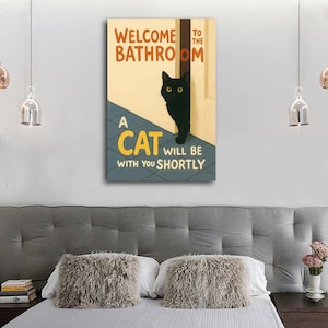 May include: A rectangular canvas print with the text "WELCOME TO THE BATHROOM" and "A CAT WILL BE WITH YOU SHORTLY." A black cat with yellow eyes peeks out from behind a door. The background is a light beige with a blue and gray floor.