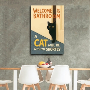 May include: A rectangular canvas print with the text "WELCOME TO THE BATHROOM" and "A CAT WILL BE WITH YOU SHORTLY." A black cat with yellow eyes peeks from behind a door. The background is a light beige and blue.