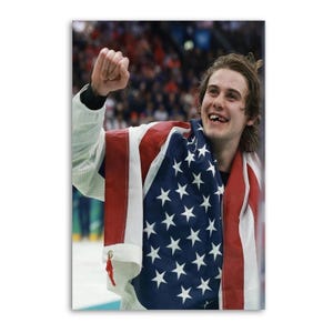 May include: A smiling person draped in an American flag, celebrating a victory. The flag features red and white stripes and white stars on a blue background. The person is wearing a white jacket and has their fist raised in the air.