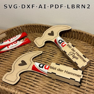Op de afbeelding: Twee houten hamervormige geschenkdozen met een hartontwerp en de tekst "du bist der Hammer Papa". De dozen bevatten chocoladerepen. De afbeelding bevat ook de tekst "SVG DXF AI PDF LBRN2".