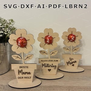 Może przedstawiać: Drewniane dekoracje w kształcie kwiatów z czerwono-złotym cukierkowym środkiem, każda w podstawie doniczki. Tekst na doniczkach brzmi "BESTE Mama DER WELT", "ALLES LIEBE ZUM Muttertag" i "für Mama". Obraz zawiera również tekst "SVG.DXF.AI.PDF.LBRN2".