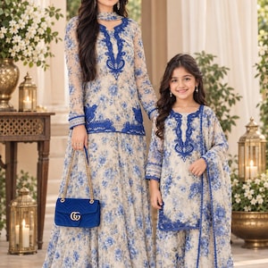 May include: Two matching outfits featuring a beige base with a blue floral pattern. The adult outfit includes a long-sleeved tunic with blue lace trim and a floor-length skirt. The child outfit includes a tunic with blue lace trim and matching pants.