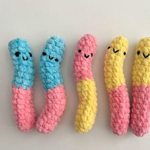Puede incluir: Seis gusanos de peluche sonriendo. Dos son azules y rosas, dos son amarillos y rosas y dos son azules y rosas. Cada gusano tiene una cara sonriente con ojos negros y una boca curvada. Los gusanos están hechos de un material suave y texturizado.