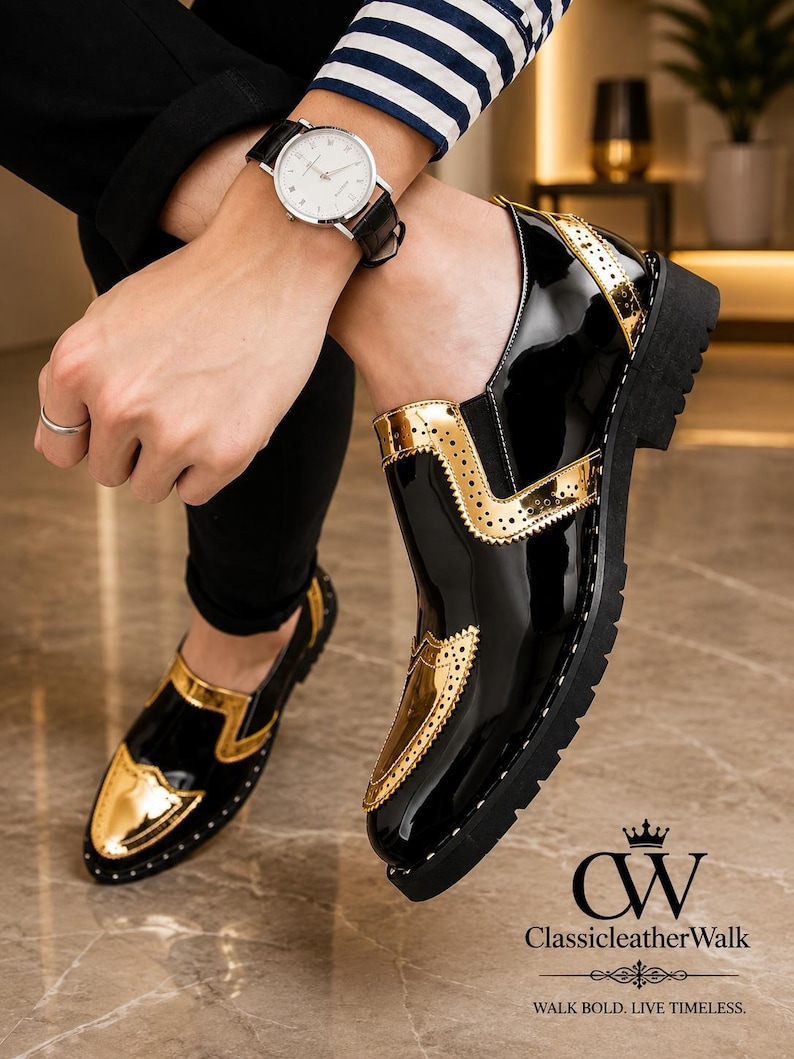 Op de afbeelding: Een paar zwarte en gouden lakleren loafers met een wingtip-ontwerp met decoratieve perforaties, een dikke zwarte profielzool en een glanzende afwerking. De schoenen zijn geaccentueerd met metallic gouden panelen op de neus en zijkant.