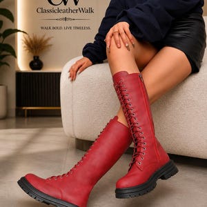 May include: Knee-high red leather boots featuring a front lace-up design with silver eyelets, a side zipper closure, and a thick black lug sole. The logo ClassicLeatherWalk and the text WALK BOLD. LIVE TIMELESS. appear in the upper left corner.
