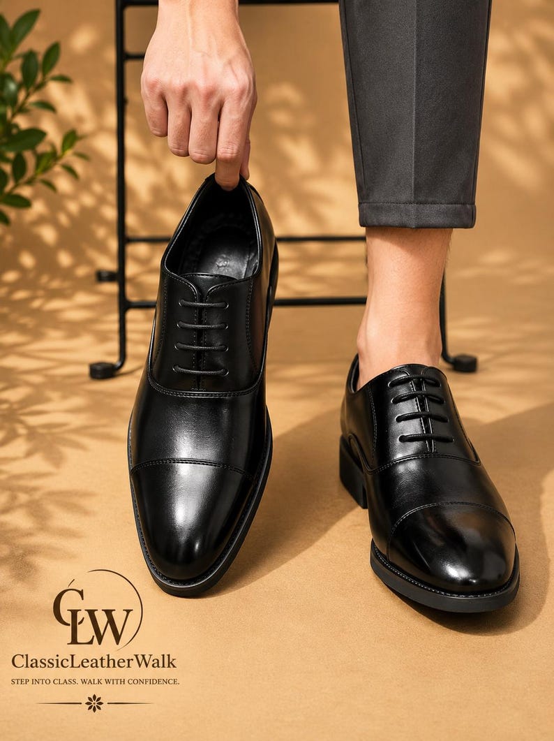 May include: A pair of black leather oxford shoes featuring a cap toe design, tonal black laces, and a low heel. The shoes have a smooth, polished finish and a structured silhouette. The logo ClassicLeatherWalk is printed in the bottom left corner.