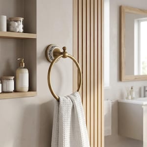 May include: A brass-coloured towel ring with a floral pattern on the wall fitting. A white waffle-textured towel is draped on the ring. The bathroom accessory is mounted on a neutral wall, with a wooden slatted panel in the background.