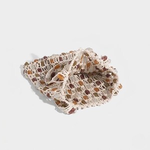 May include: A beige crocheted bag with a grid-like pattern, filled with various-colored stones. The stones are in shades of brown, orange, and white. The bag is folded over, revealing the interior and the stone contents.