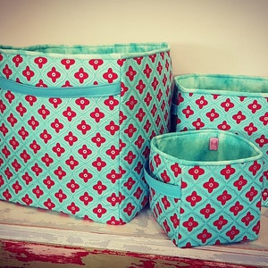 Puede incluir: Tres cestas de almacenamiento de tela turquesa con patrones florales rojos. Las cestas están anidadas una dentro de la otra, con la cesta más grande en la parte inferior y la cesta más pequeña en la parte superior.
