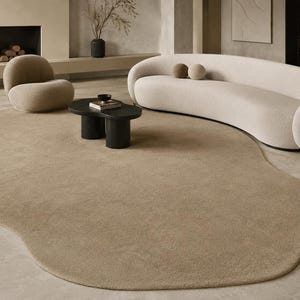 May include: A large, beige, organic-shaped area rug with a soft, textured surface. The rug features an irregular, rounded perimeter that curves across the floor, providing a neutral foundation for the surrounding furniture and decor items.